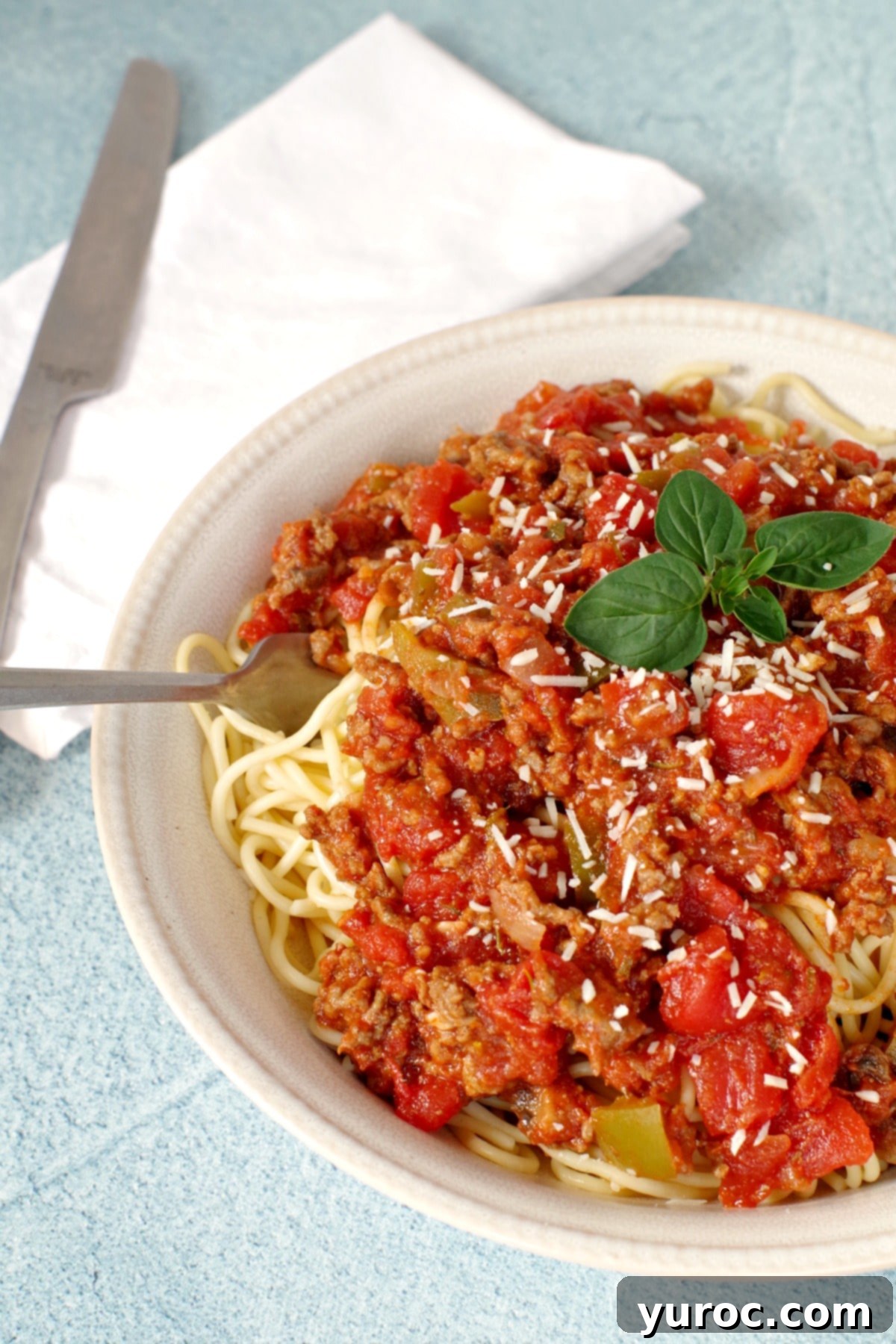 Close-up of a serving of spaghetti and meat sauce in a beige bowl, ready to be enjoyed