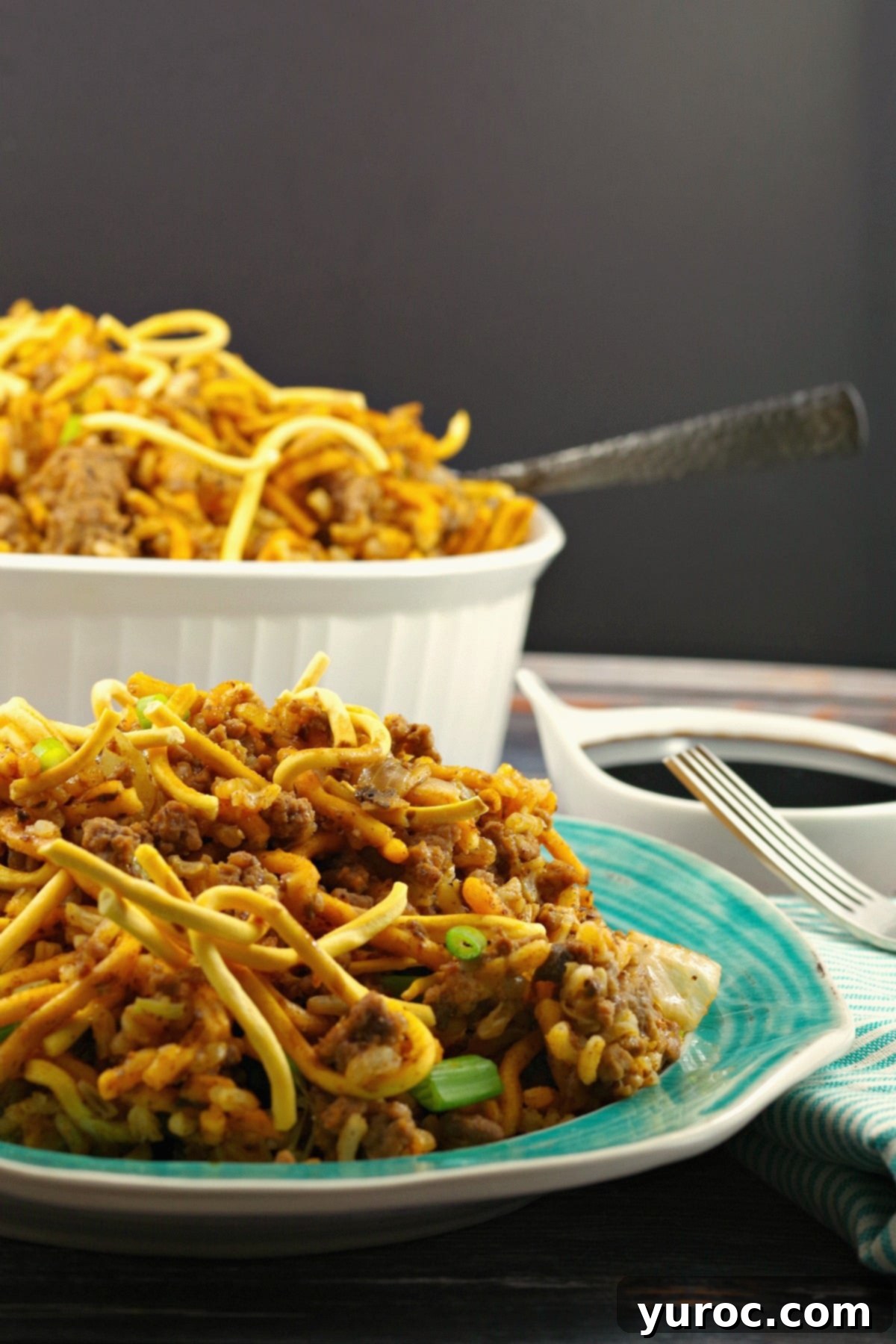 Hearty Chow Mein Hotdish 12 A serving of Chow Mein Hotdish on a plate, with the full casserole dish in the background, adorned with green onions and crispy noodles.