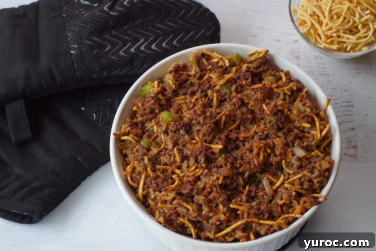 Hearty Chow Mein Hotdish 10 Freshly baked Chow Mein Hotdish, still uncovered, on a trivet, with extra dry chow mein noodles and oven mitts nearby.