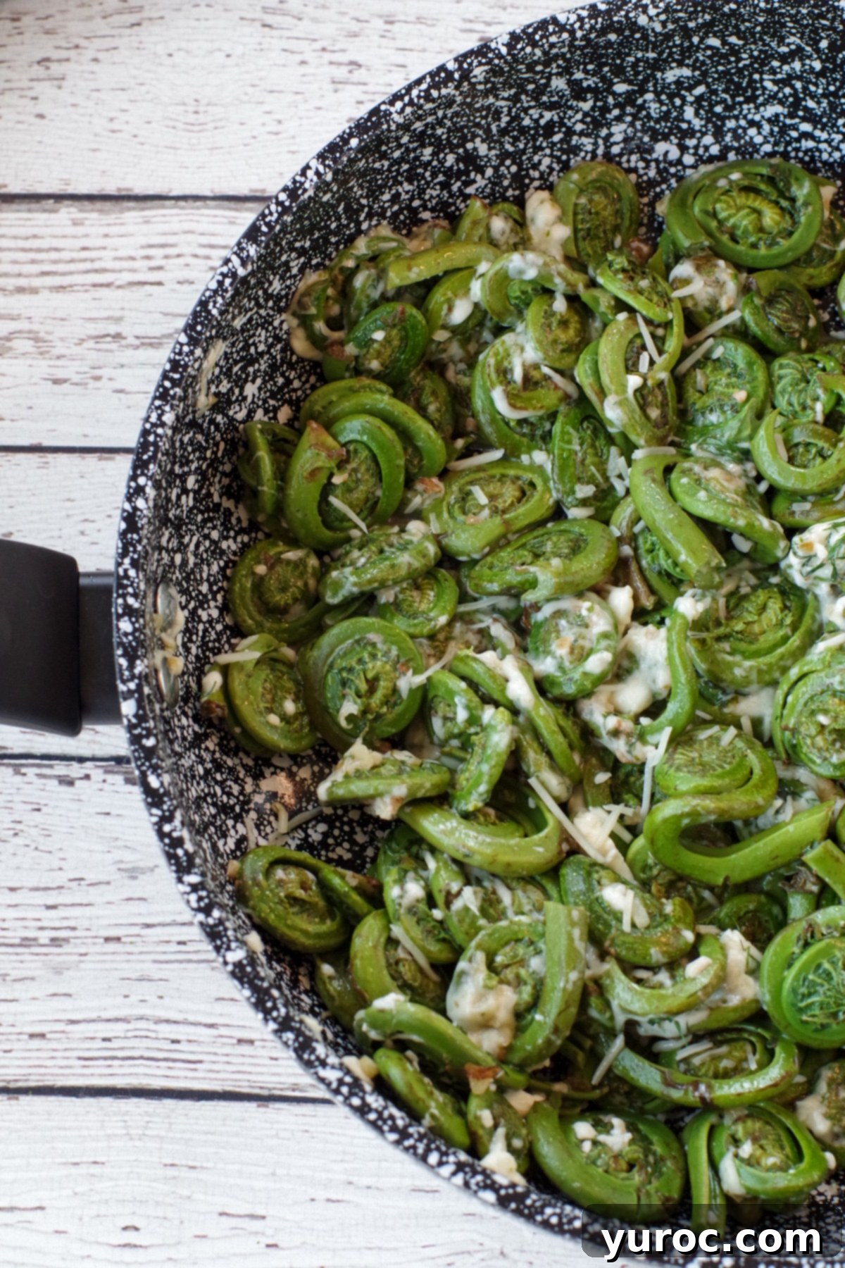a half pan of sauteed fiddleheads on a white faux wooden surface