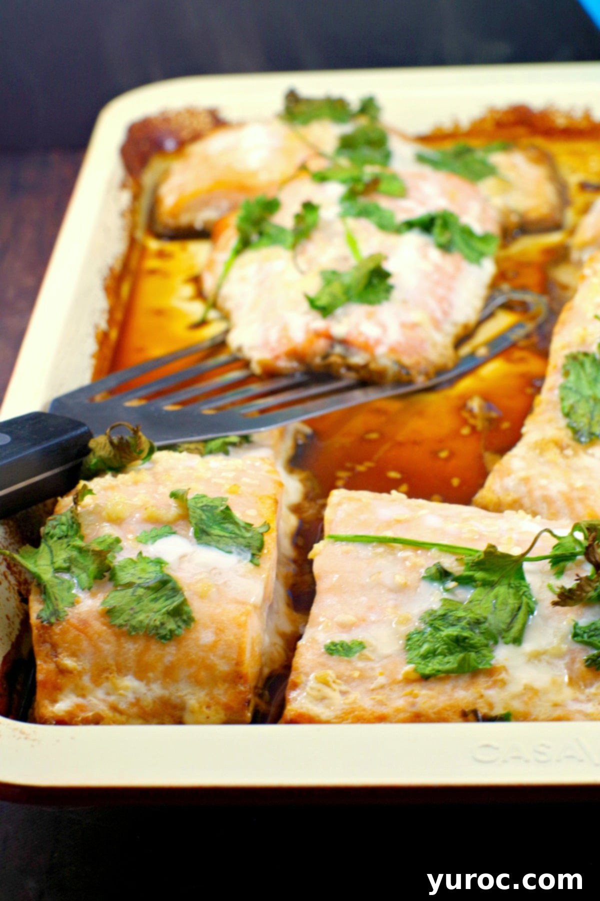 Cooked frozen salmon fillets on a sheet pan, with one serving being lifted onto a plate.
