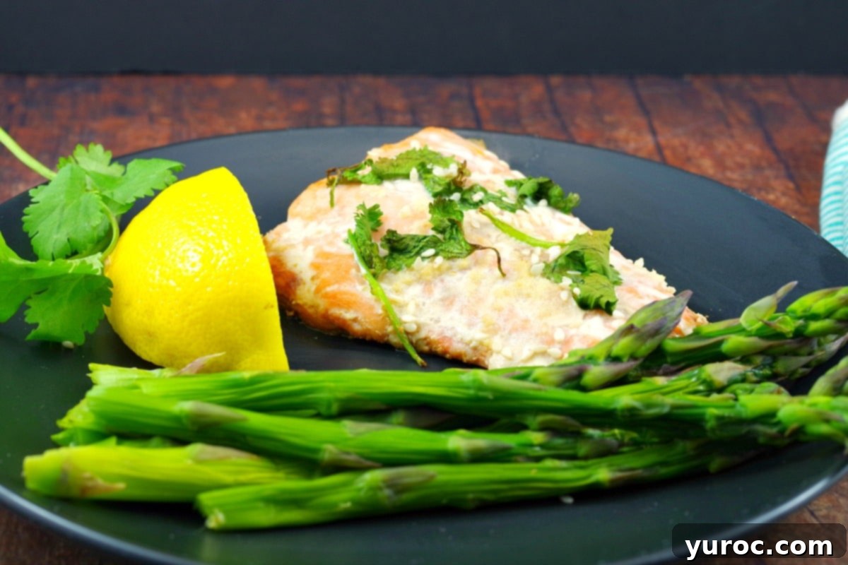A perfectly cooked salmon fillet on a black plate, garnished with a lemon wedge and served alongside steamed asparagus.