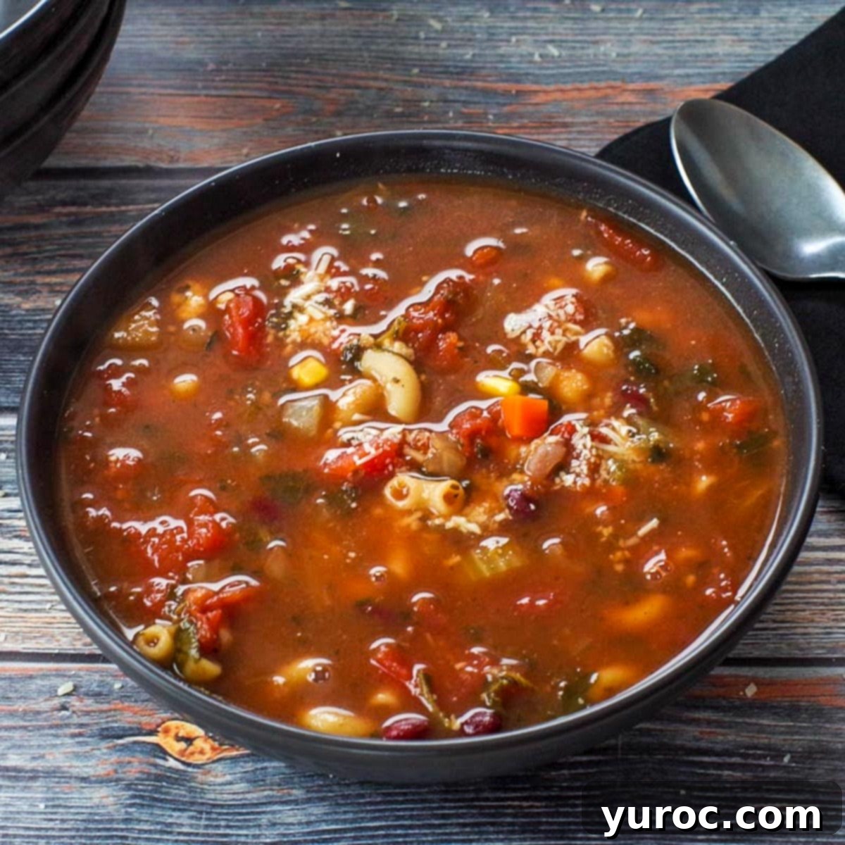 Minestrone soup in a black bowl with spoon and black napkin on the side