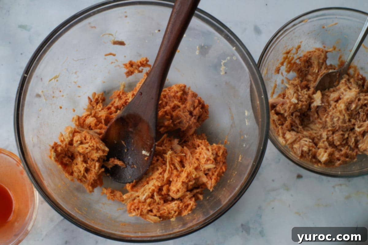 Shredded buffalo chicken with sauce in a large glass bowl and a medium glass bowl with shredded BBQ chicken.