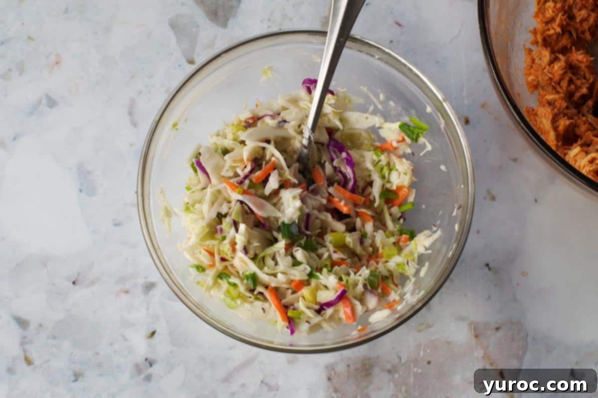 Coleslaw ingredients mixed together in a glass bowl with a spoon.