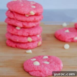 Dreamy Strawberry Milkshake Cookies 9 strawberry milkshake cookies on a wood cutting board, with a stack of cookies background and white chocolate chips scattered