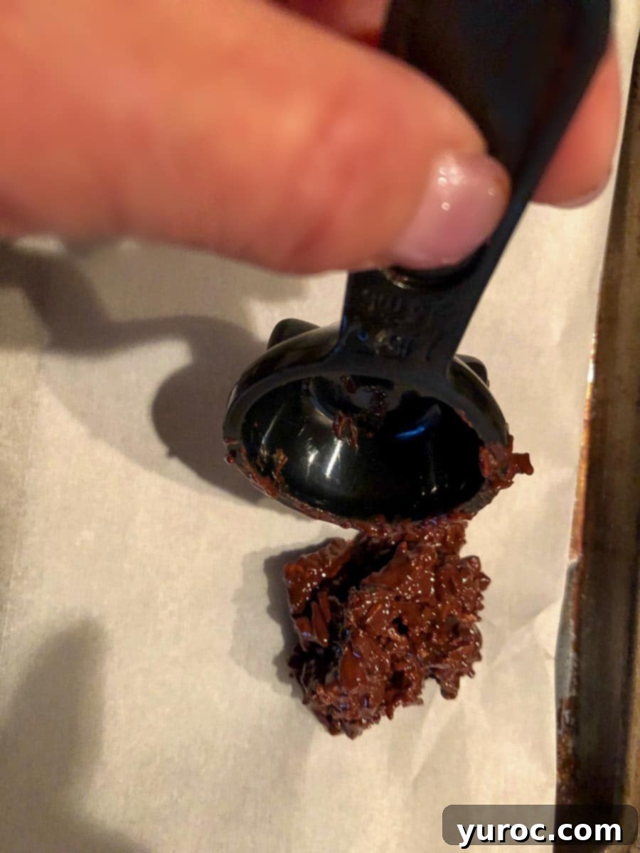Chocolate clusters being dropped from a tablespoon onto a parchment-covered baking sheet.