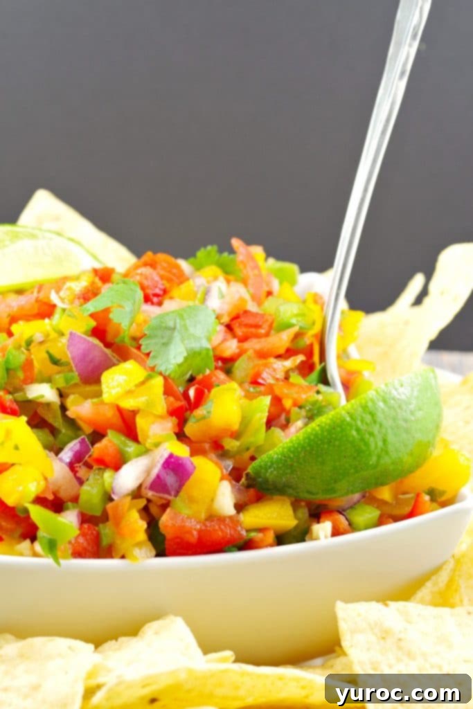 Bright & Zesty Pico de Gallo 4 Pico de Gallo Salsa. garnished with 2 lime wedges, in a white bowl surrounded by nacho chips