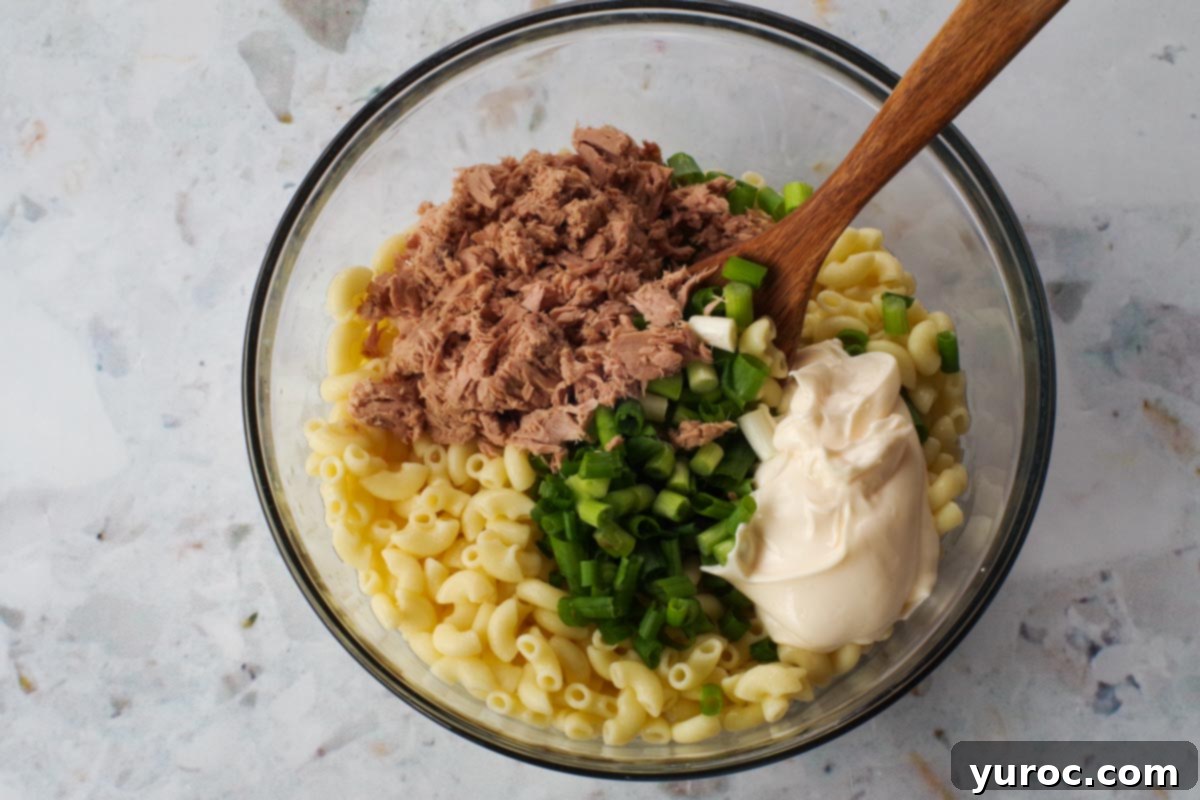 Wholesome Tuna Macaroni Salad 7 Macaroni with tuna, mayonnaise and onions in a glass bowl with a wooden spoon.