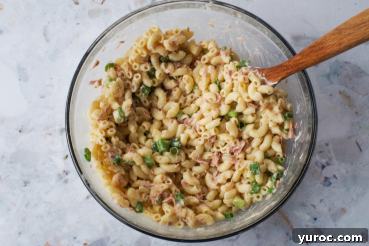 Wholesome Tuna Macaroni Salad 8 Tuna mixed together with other ingredients in a large glass bowl with a wooden spoon.