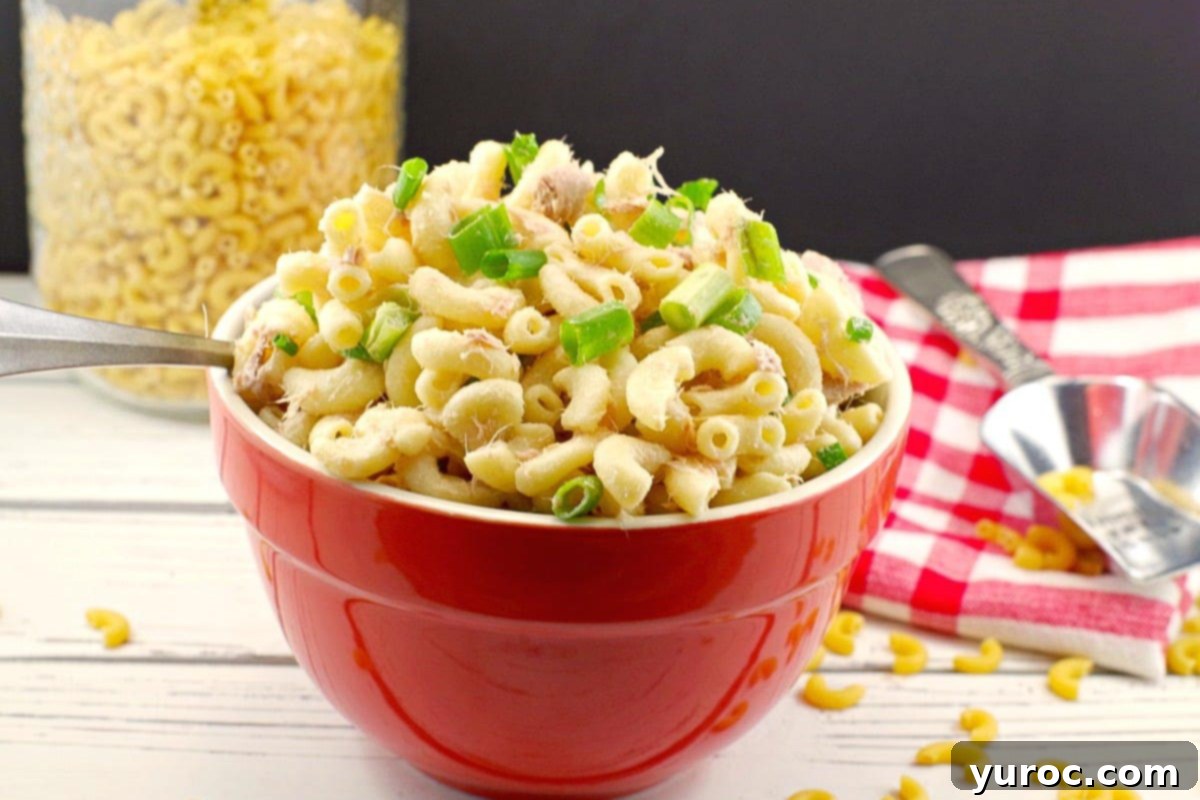 Wholesome Tuna Macaroni Salad 9 Simple tuna macaroni salad in a red serving bowl with a jar of dry macaroni in the background.