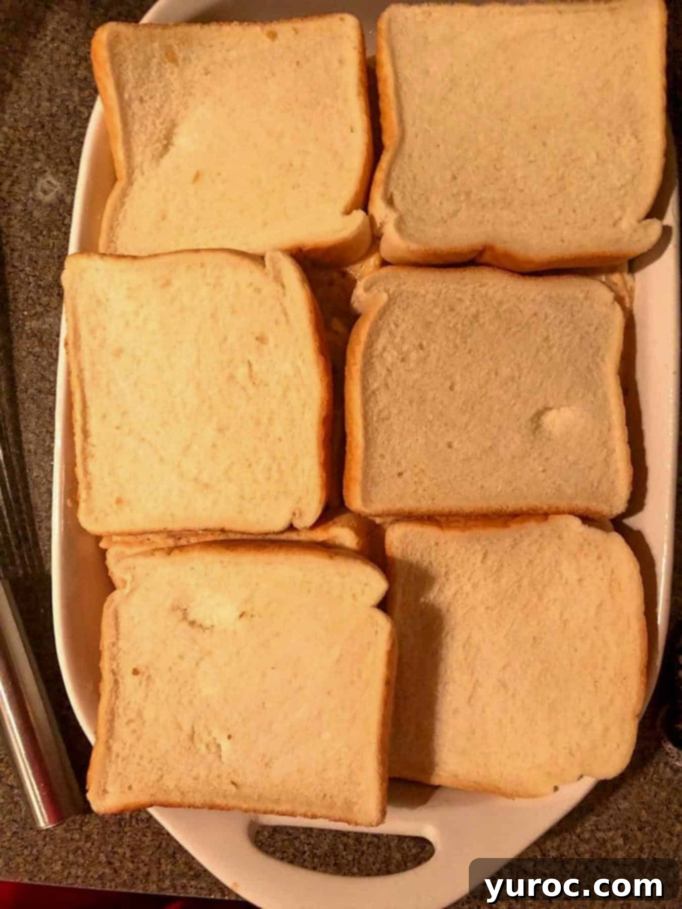 The second layer of thick bread slices is carefully placed over the first soaked layer in the white casserole dish, creating a double-layered foundation for the French toast casserole.