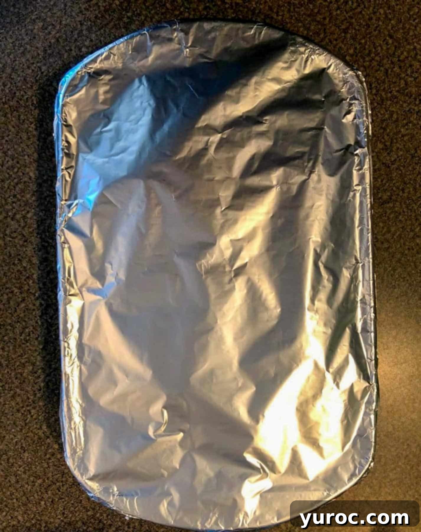 A white casserole dish filled with the prepared carrot cake French toast mixture is covered tightly with aluminum foil, ready for refrigeration overnight.
