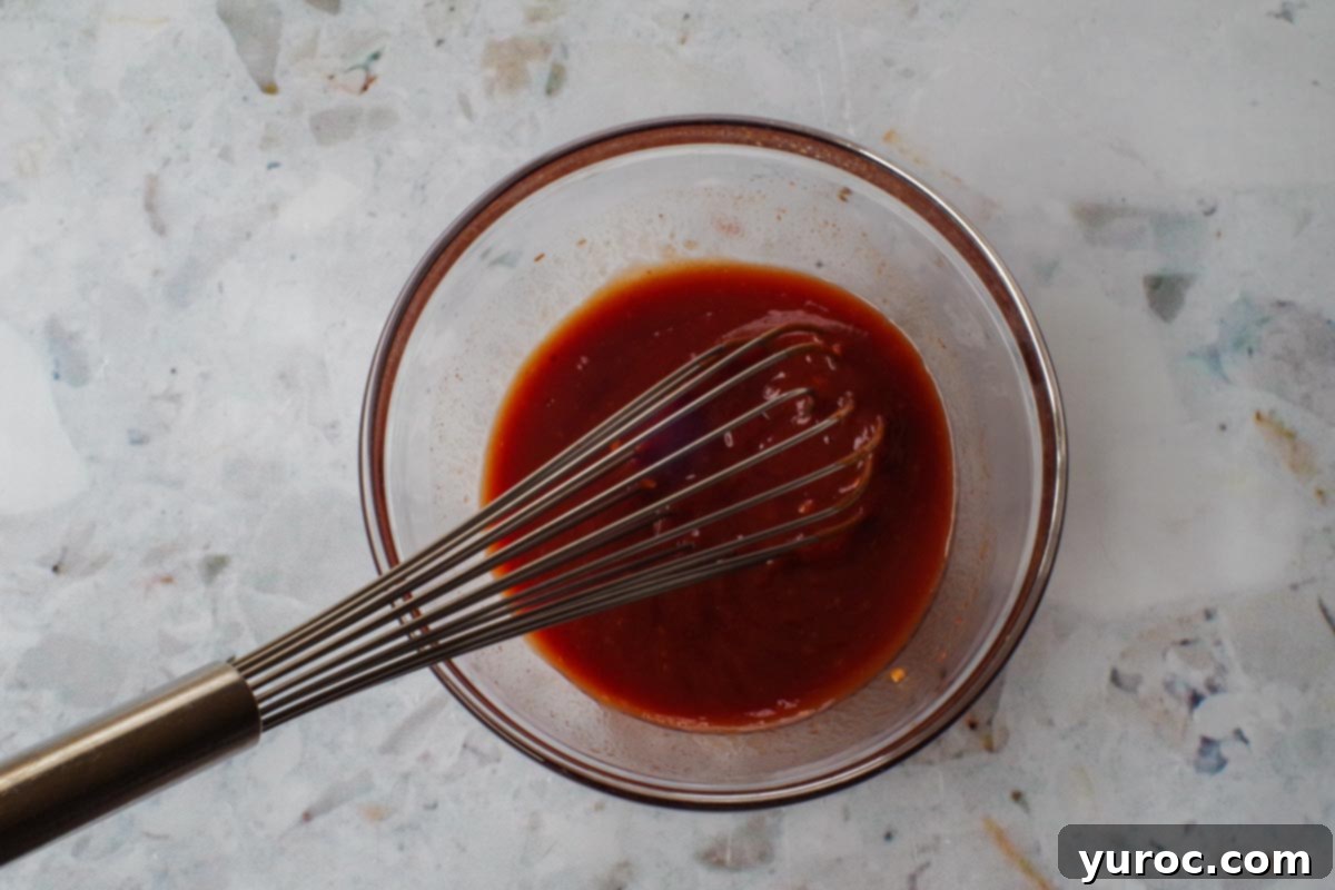 Quick and Easy Ketchup Brown Sugar BBQ Sauce 5 Ingredients in Barbeque sauce with ketchup and brown sugar thoroughly mixed together in a glass bowl with a large metal whisk, showcasing the smooth consistency.