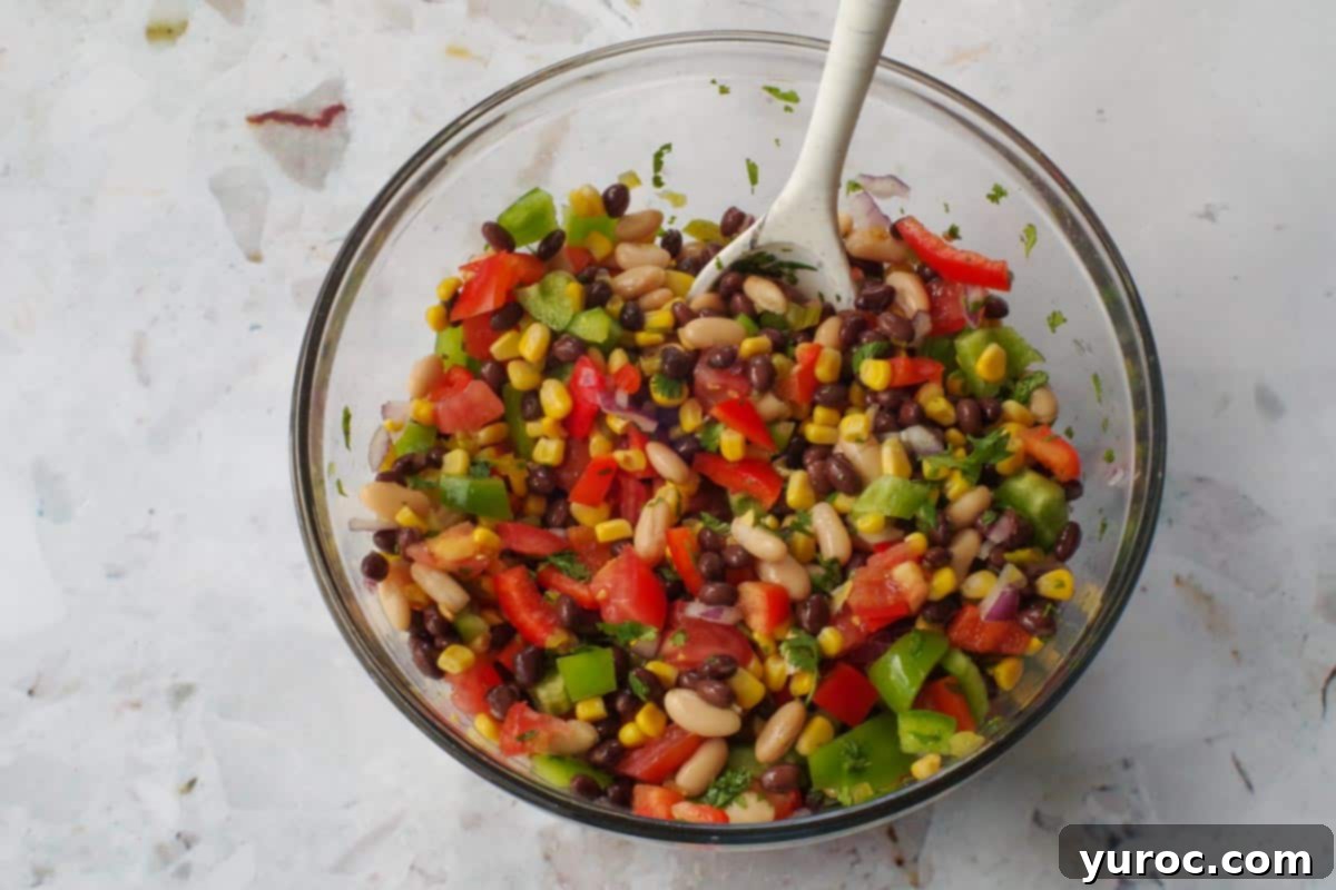 Ingredients in cowboy caviar in a large glass bowl with a spoon.
