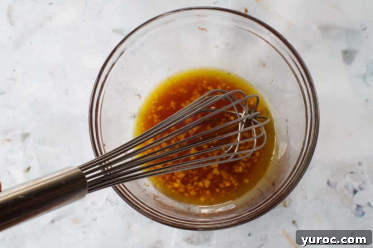Dressing ingredients mixed together in medium glass bowl with a large metal whisk.