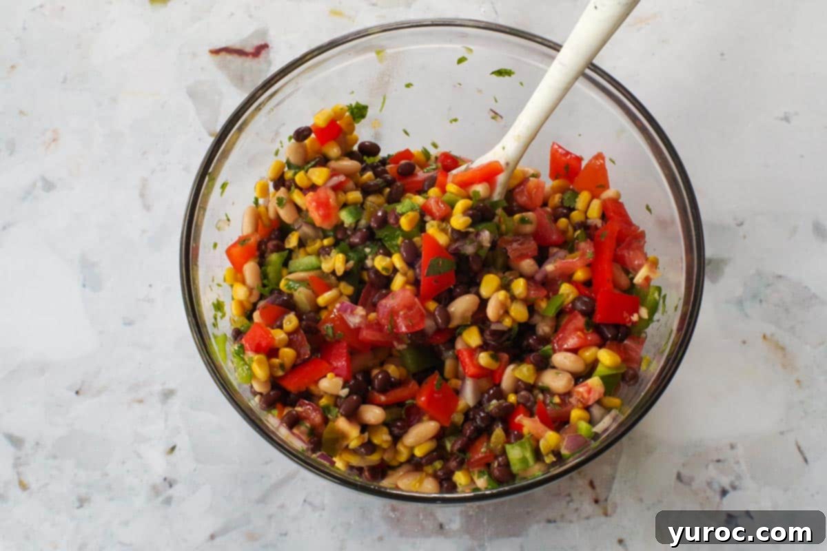Cowboy Caviar with dressing mixed in, in large glass bowl with marble silicone spoon.