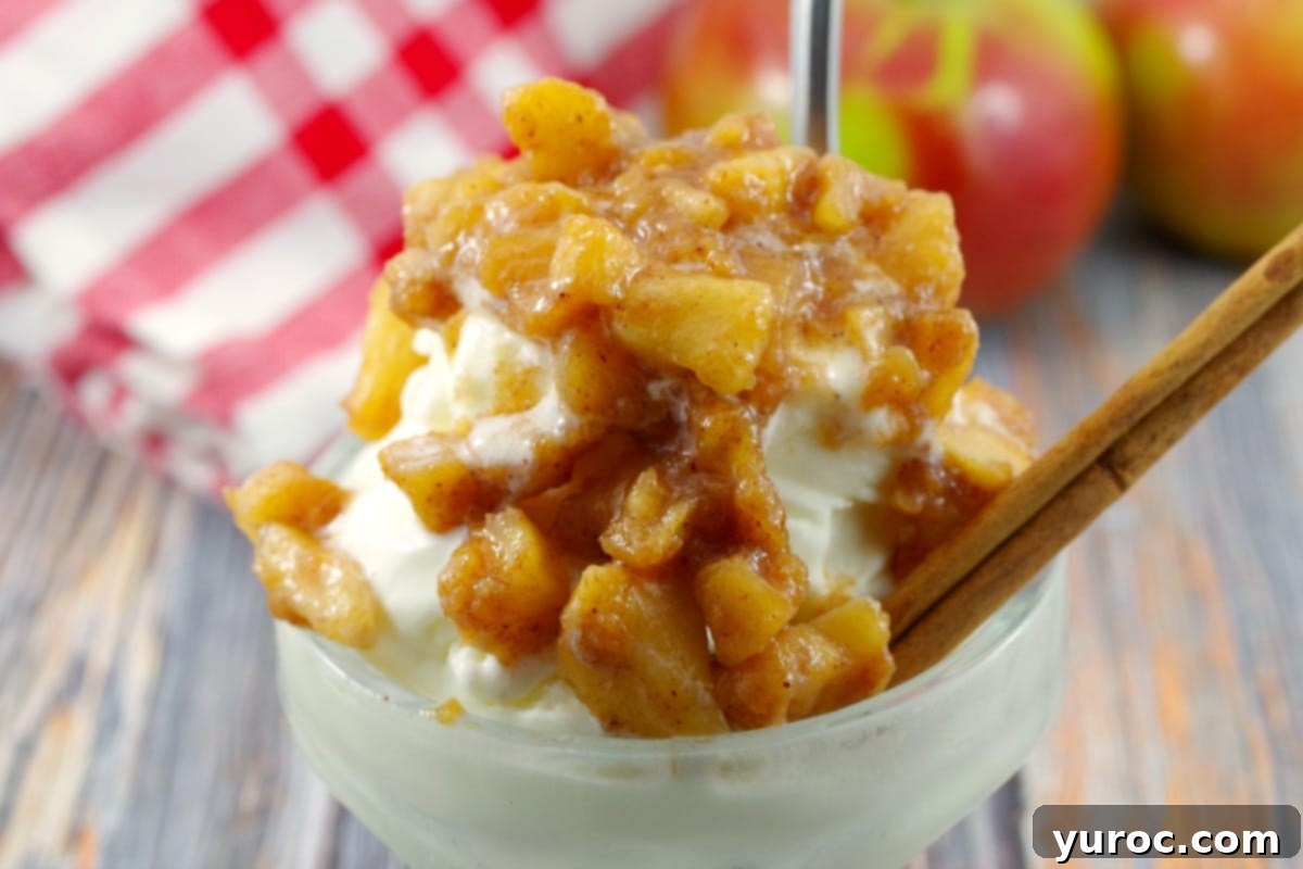 Warm Apple Cinnamon Topping 1 Apple cinnamon topping on frozen yogurt in an ice cream dish with a spoon, cinnamon stick, fresh apple, and checkered cloth in the background, highlighting its delicious serving suggestion.
