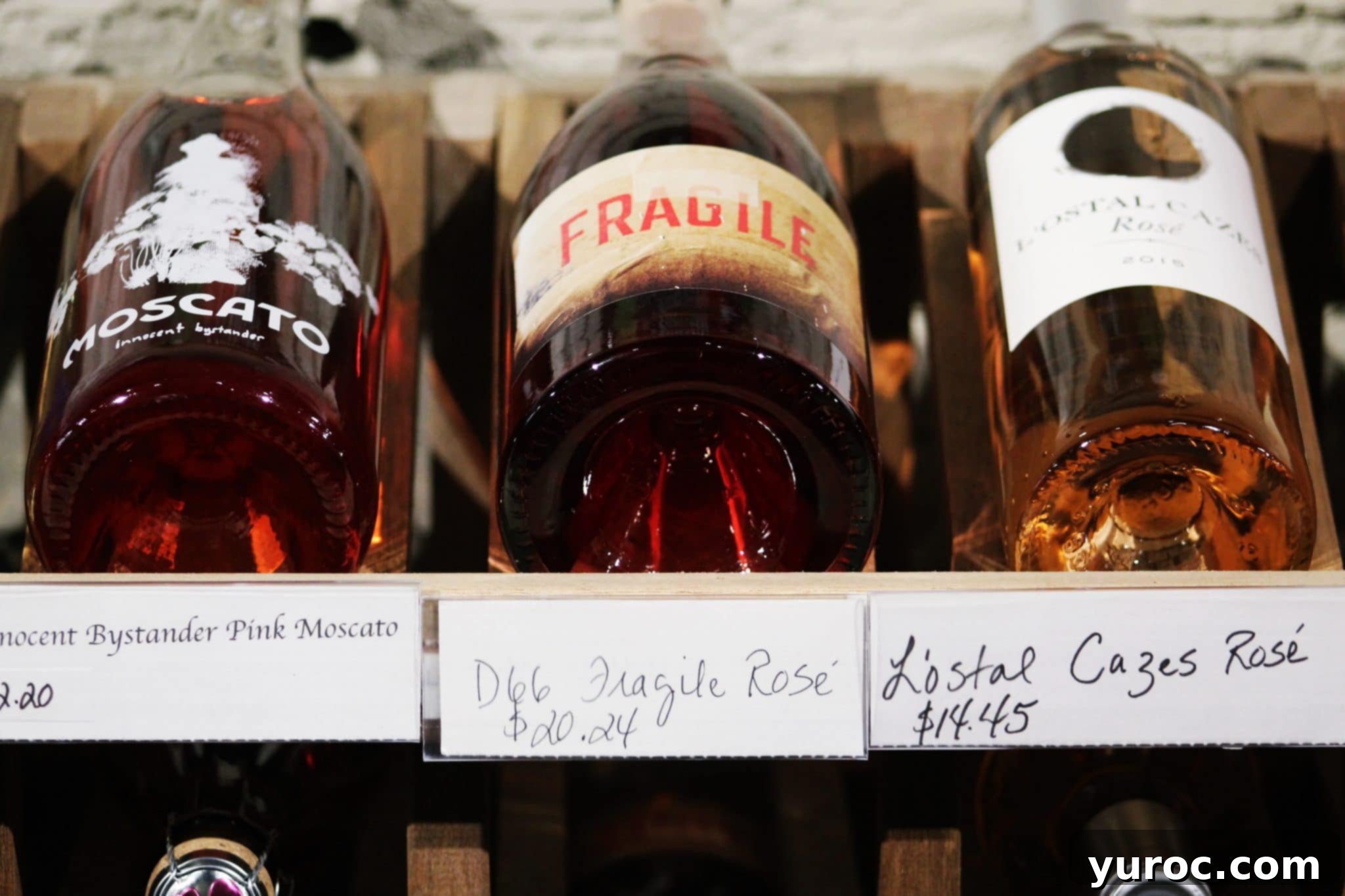 3 wine bottles, laying flat, with price tags, on a store shelf