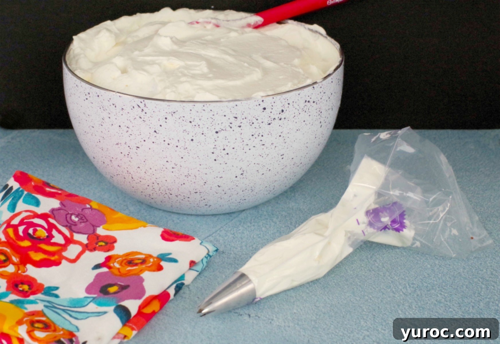 Whipped cream frosting in bowl with filled pastry bag in front, ready for decorating