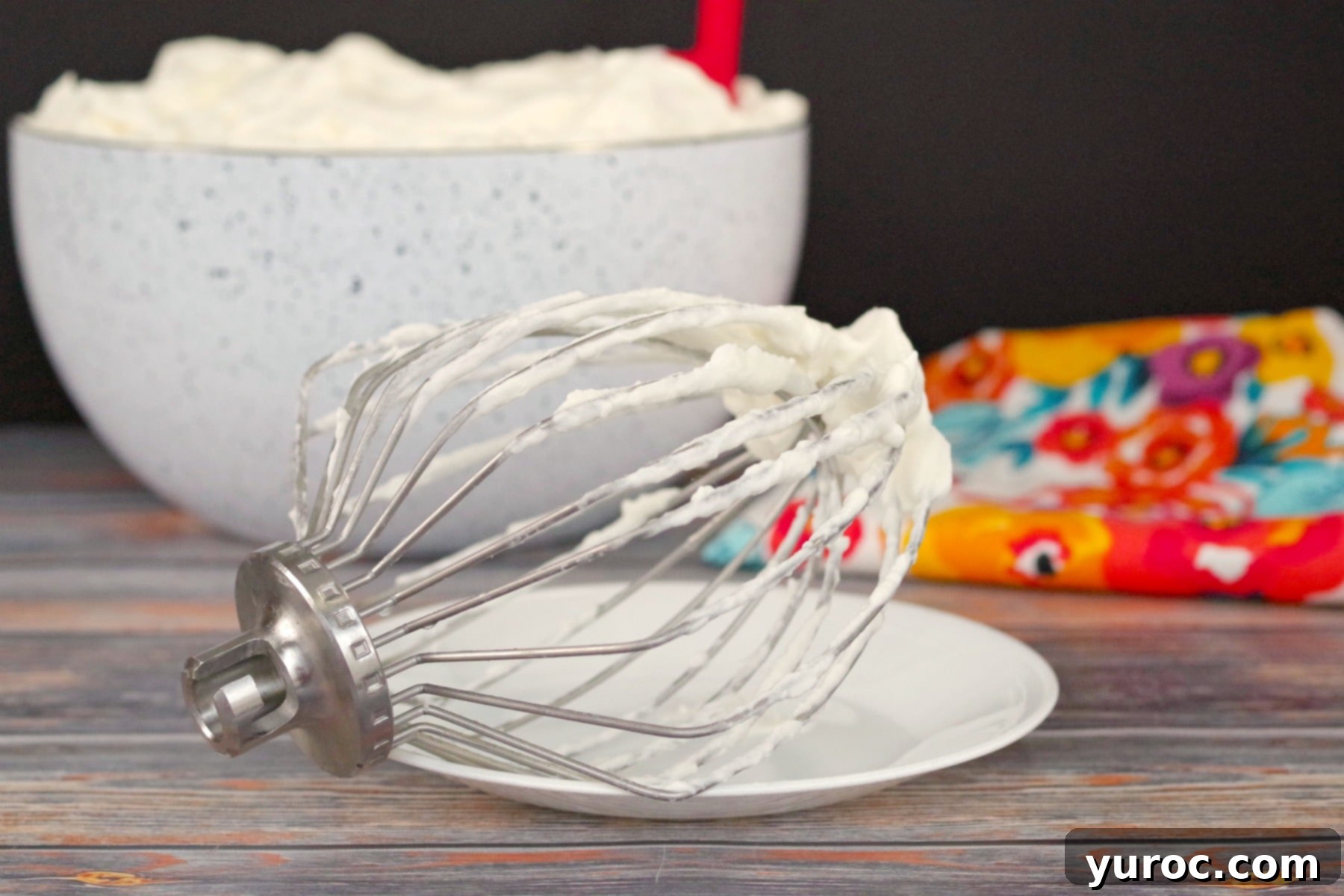 whipped cream icing in bowl with beater in front, showing stiff peaks