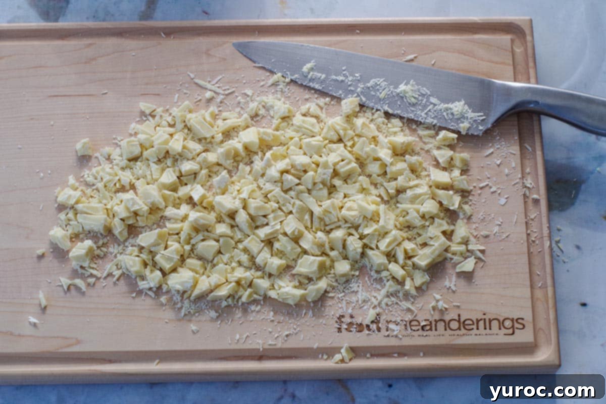 White chocolate baking bars expertly chopped into small, even pieces on a cutting board, with a chef's knife beside them.