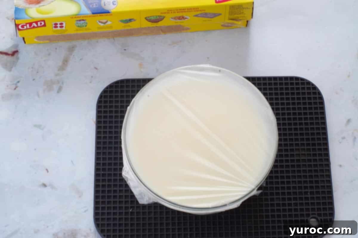 The white chocolate whipped cream mixture in a glass bowl, tightly covered with a layer of Glad Press 'n Seal plastic wrap, prepared for chilling.