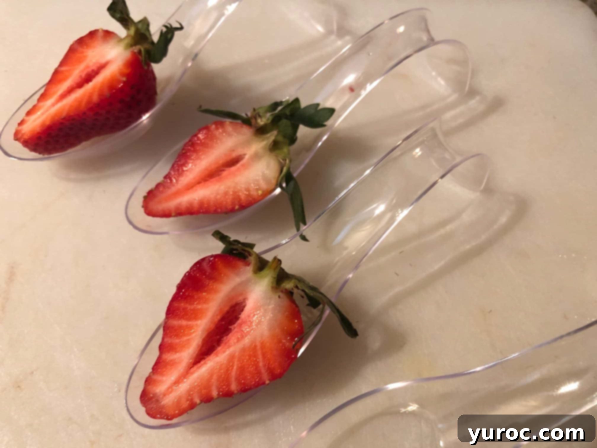 Half a strawberry with the sliced side facing up and stem still attached, placed at the bottom of a small dessert spoon.