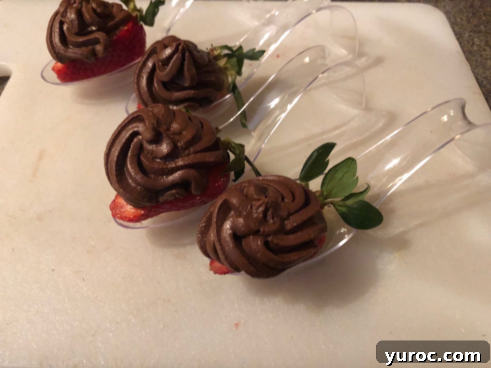 A dollop of chocolate avocado mousse expertly piped onto a strawberry half resting on a spoon, resembling a mini cupcake.