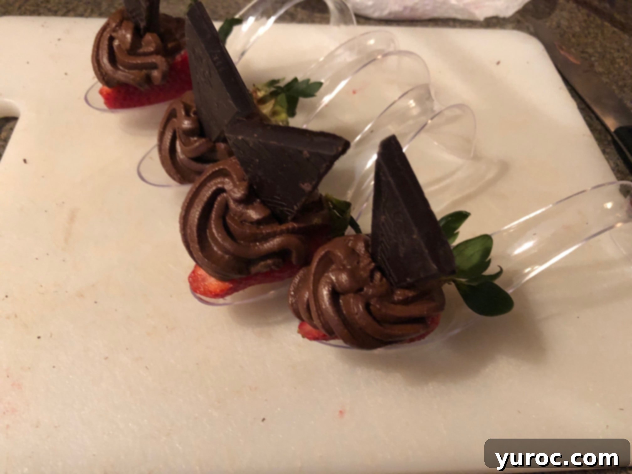 A small piece of dark chocolate delicately placed into the center of the piped chocolate avocado mousse on a strawberry spoon dessert.