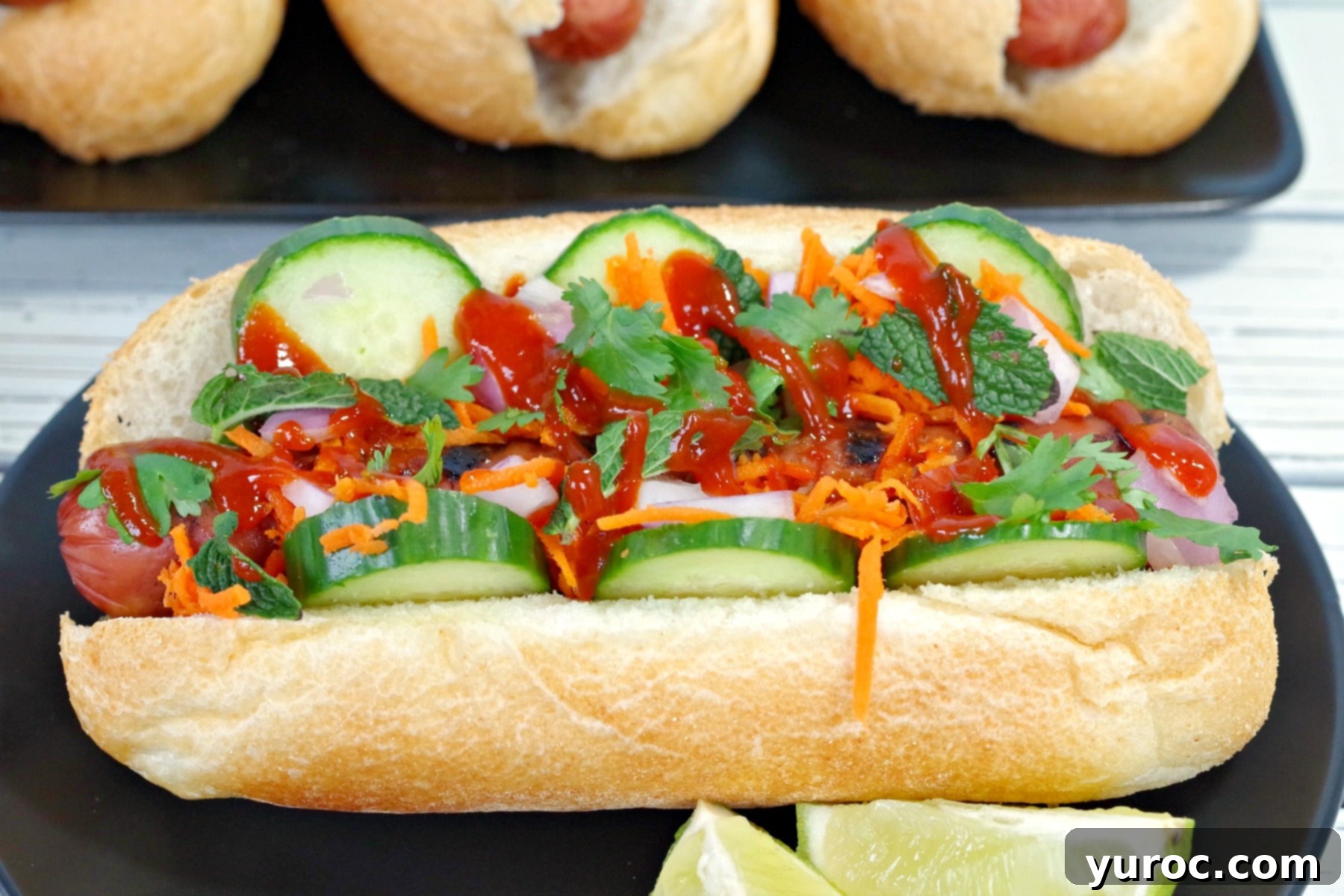 Banh Mi Turkey Hot Dog Twist 4 Side view of Banh Mi Turkey Hot dog on black plate with lime wedges, highlighting the layers of fresh toppings.