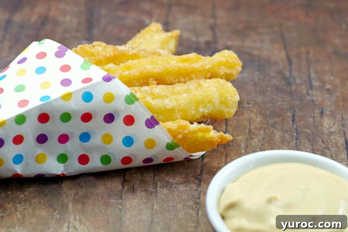 Churros in a paper polka-dot holder layer on a a wooden surface beside a bowl of dulce de leched dip.