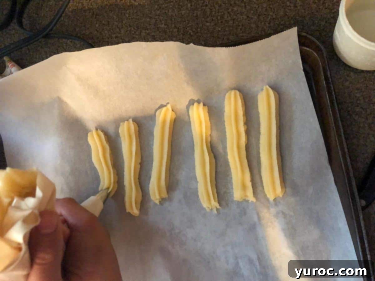 Churros being piped onto parchment lined baking tray.