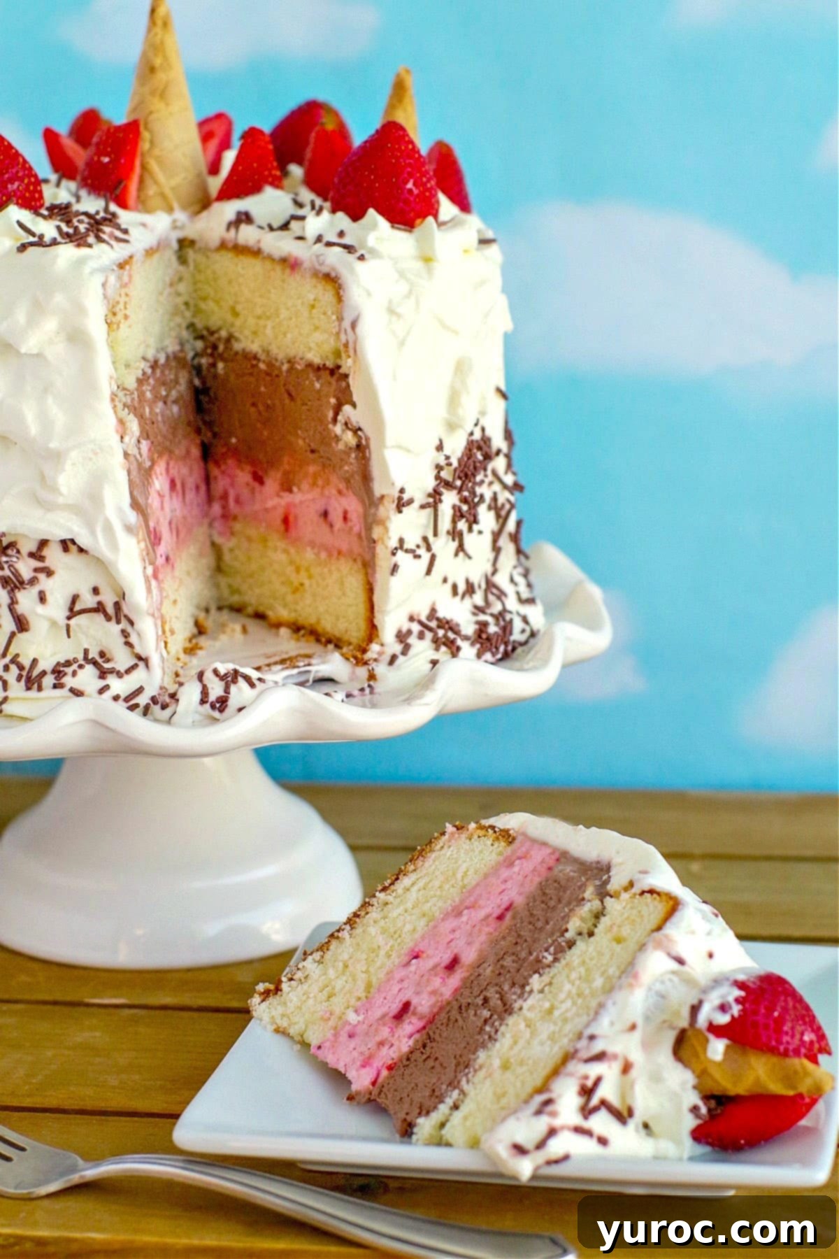 Decadent Neapolitan Ice Cream Cake 2 A beautiful slice of Neapolitan Ice Cream cake on a white plate, with the whole cake on a white cake stand in the background, showcasing distinct vanilla cake, chocolate ice cream, and strawberry ice cream layers