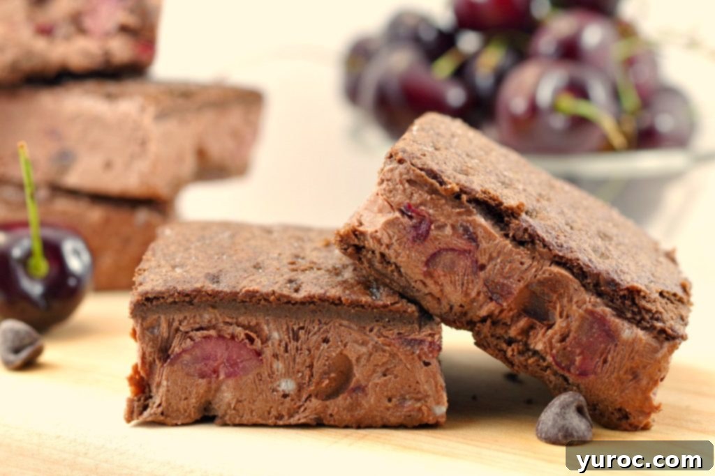 Two Weight Watchers Black Forest Ice Cream Sandwiches on a cutting board, with a bowl of fresh cherries in the blurred background, highlighting their tempting appearance.