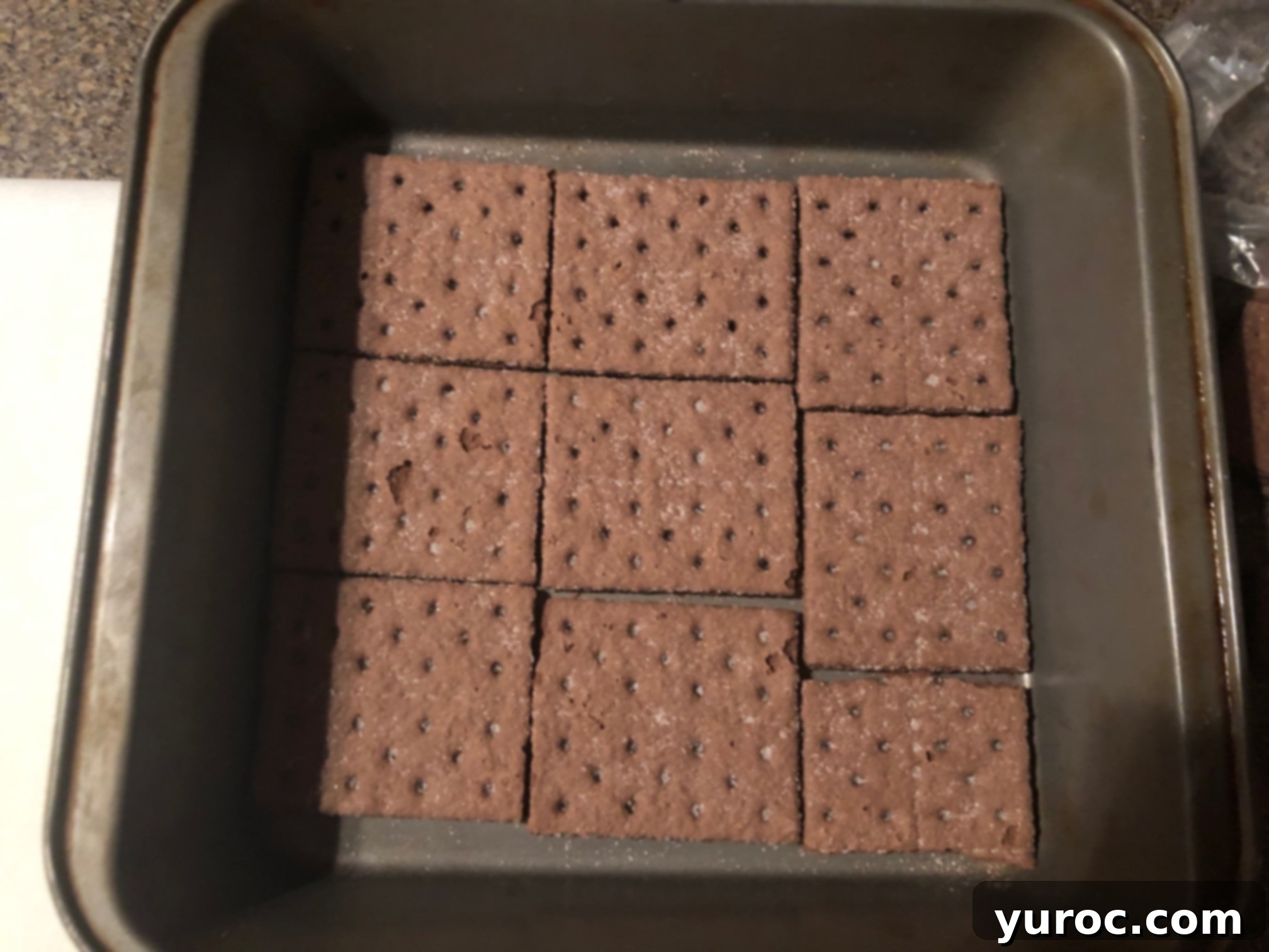 A baking pan neatly lined with chocolate graham crackers, forming the base of the ice cream sandwiches.
