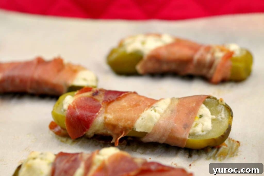 Creamy Boursin Pickle Bites 2 Golden-brown prosciutto-wrapped Boursin stuffed pickle resting on a parchment-covered baking sheet, ready to be served