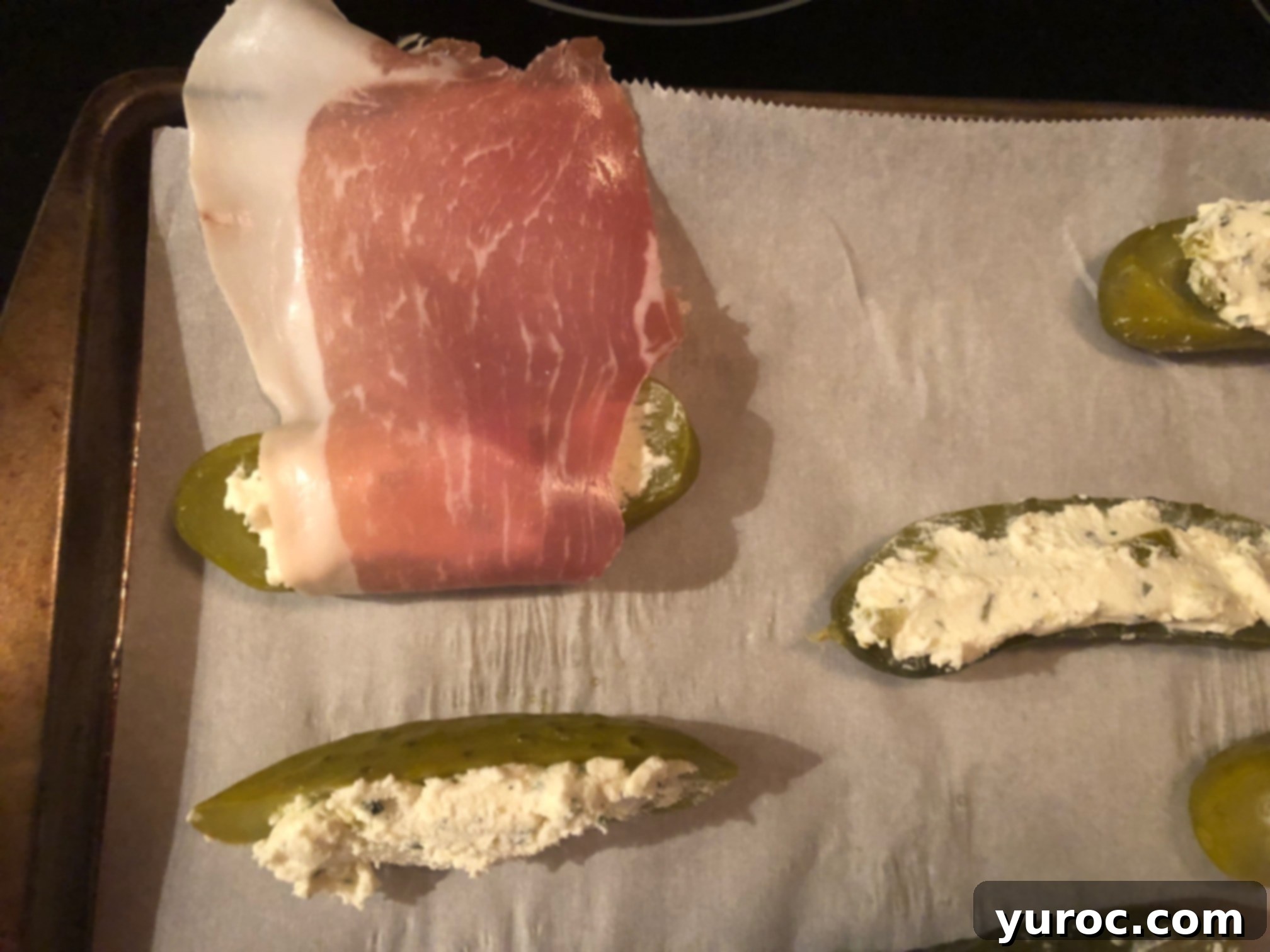 Creamy Boursin Pickle Bites 12 A strip of prosciutto being carefully wrapped around a Boursin-stuffed pickle half, covering the filling