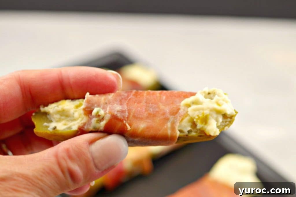 Creamy Boursin Pickle Bites 15 Close-up of a single Boursin stuffed pickle, wrapped in prosciutto, held between a thumb and forefinger, ready to be enjoyed as a perfect low-carb snack