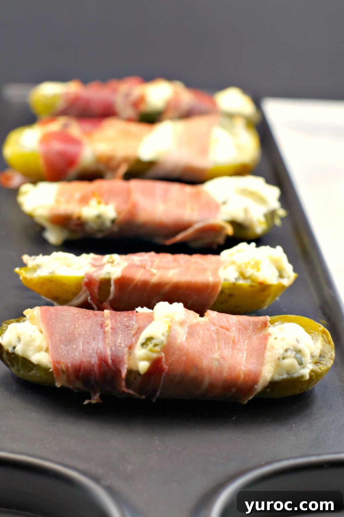 Creamy Boursin Pickle Bites 3 Crispy prosciutto-wrapped boursin stuffed pickles arranged on an elegant black serving tray, showcasing their golden-brown exterior and creamy filling, perfect for a low-carb appetizer