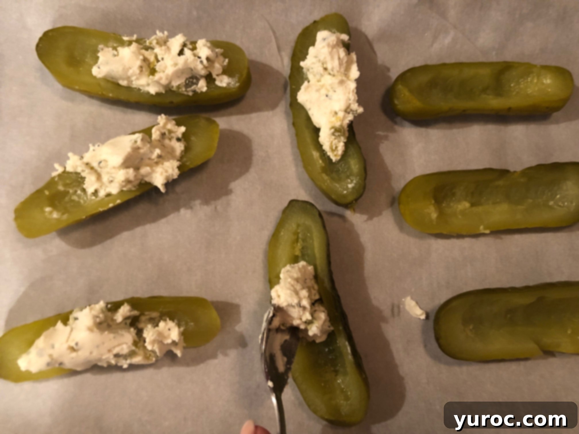 Creamy Boursin Pickle Bites 10 Pickle halves arranged on a parchment-lined baking sheet, being filled with the Boursin and jalapeño mixture using a spoon