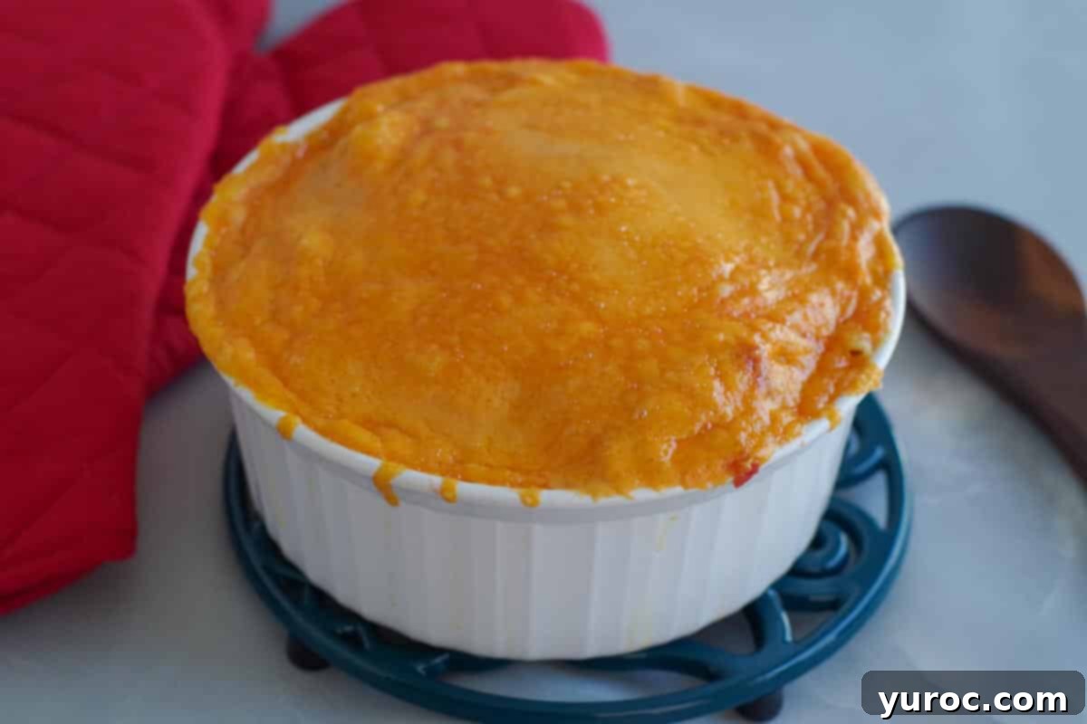 baked macaroni, cheese and tomatoes on a trivet with red oven mitts in the background