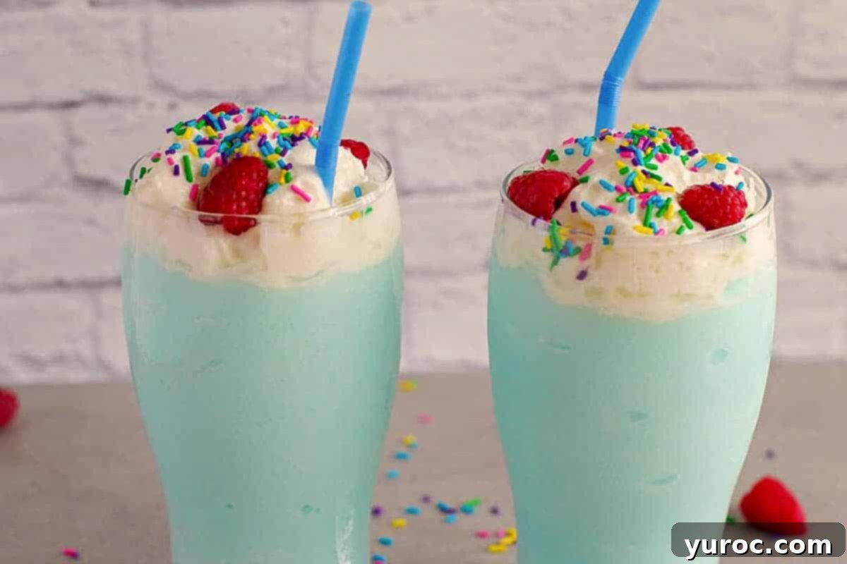 Two glasses of Creamy Coconut Blue Raspberry Slushies, garnished with whipped cream and sprinkles.