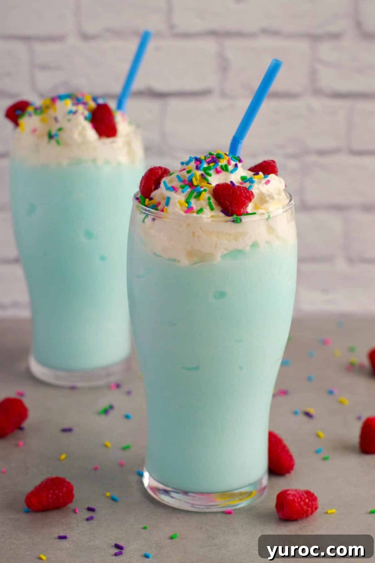 Two non-alcoholic blue raspberry drinks topped with whipped cream and sprinkles, ready to be served.