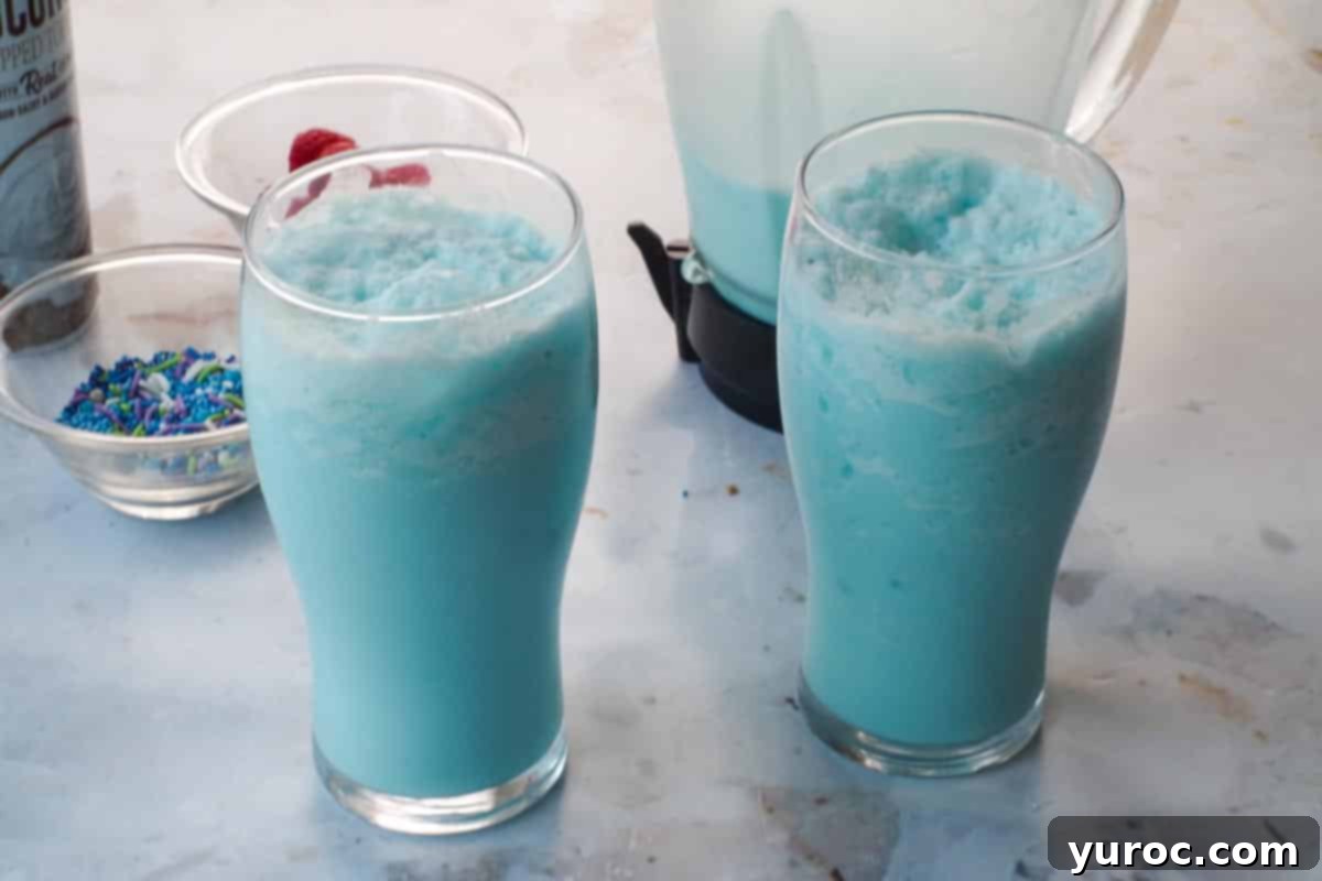 Blue raspberry slushie being poured from a blender into two serving glasses.