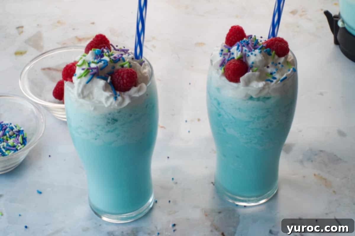 Finished Blue Raspberry Slushies garnished with whipped cream, colorful sprinkles, and fresh raspberries.