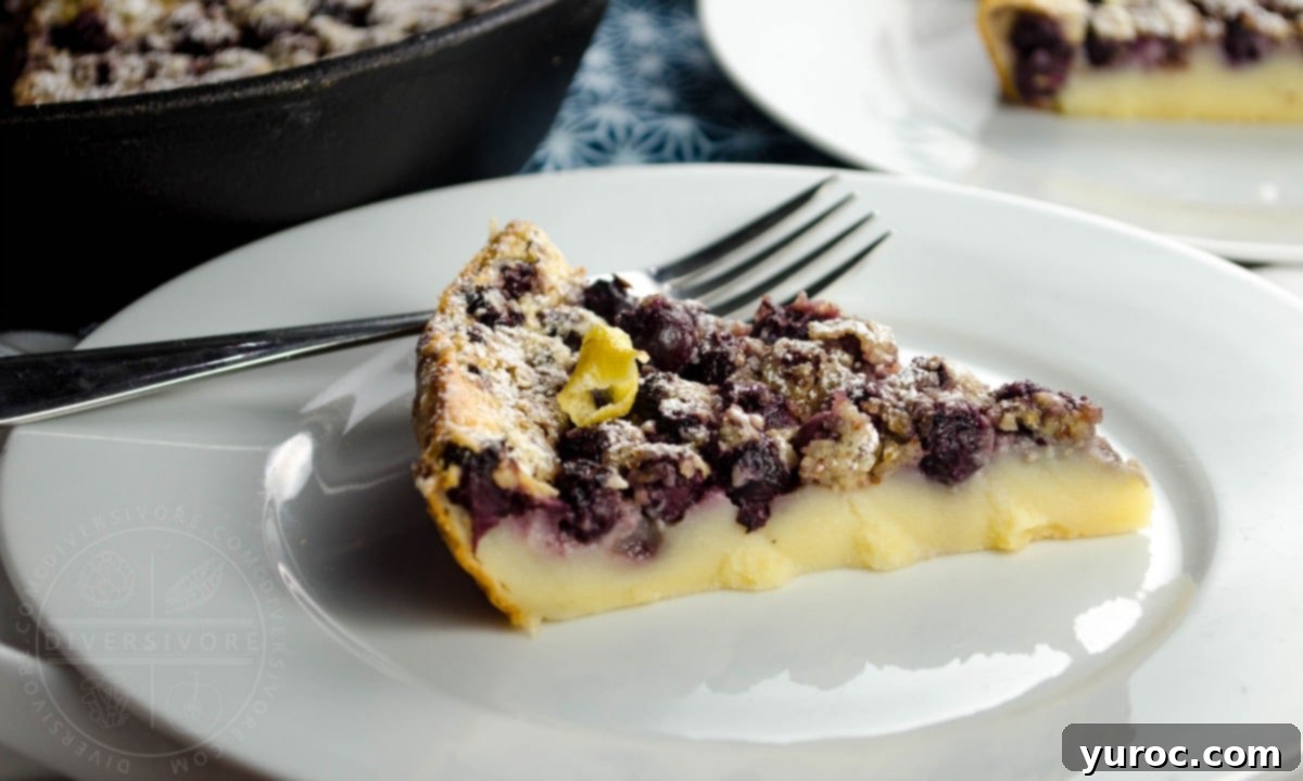 A beautifully baked Saskatoon Berry Clafoutis piece, presented on a white plate with a fork, ready for tasting.
