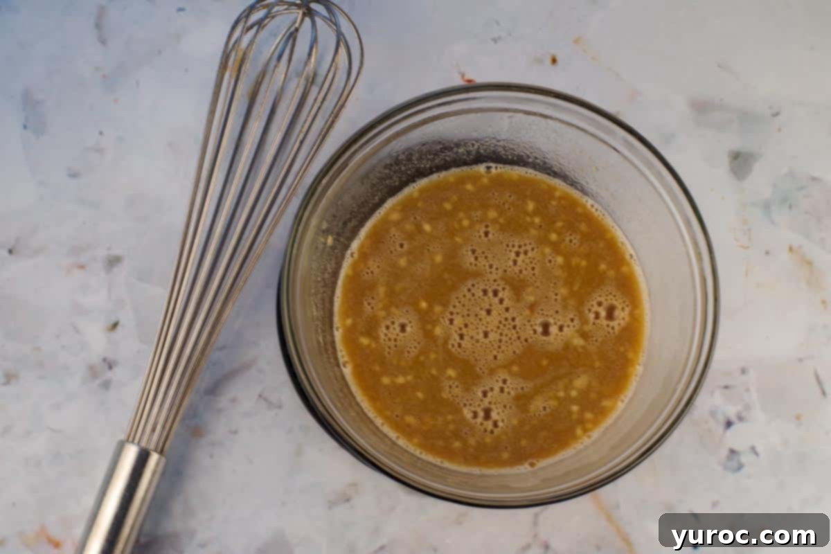 The peanut dressing ingredients, having been microwaved, are being stirred with a whisk in a glass bowl.