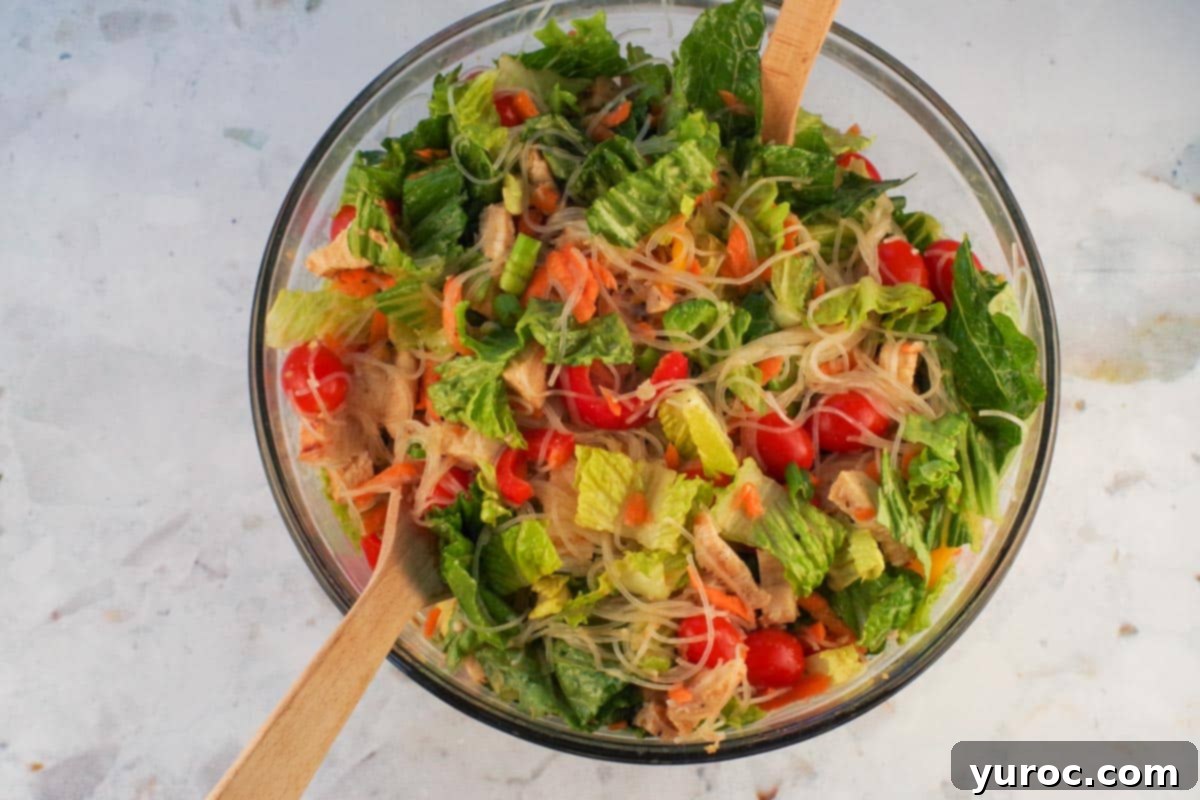 Noodles, chicken, dressing, and chopped vegetables tossed together in a large bowl, ready to serve.