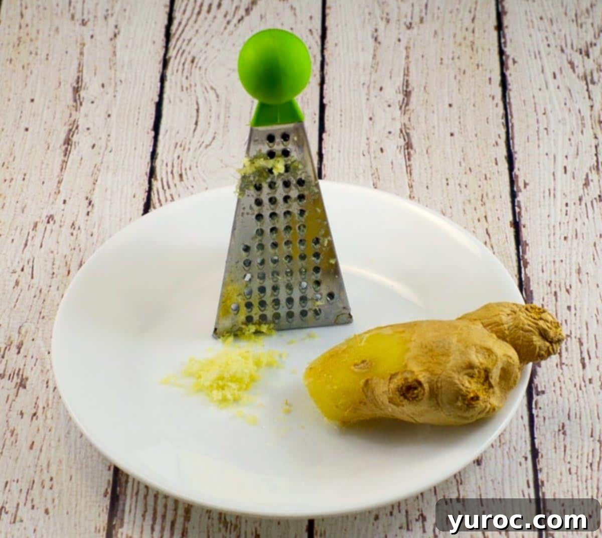 A piece of fresh ginger on a white plate with a small grater, illustrating the expert tip for storage.